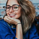 Home A young woman wearing glasses and denim, smiling in an indoor setting.