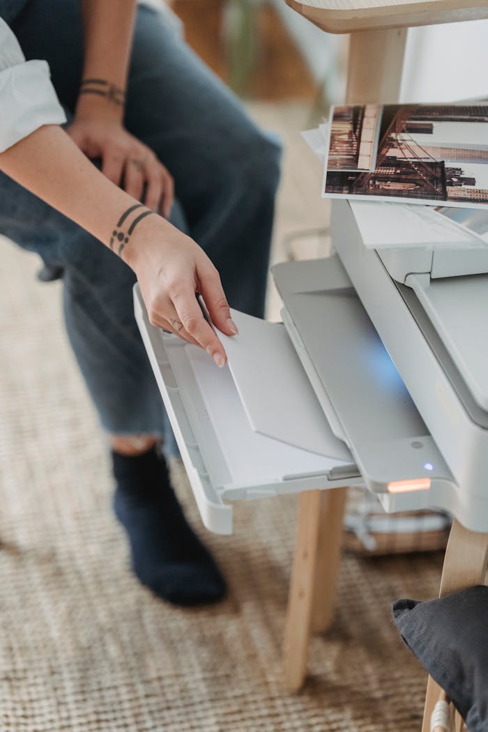 A person handling a printer in a home office setting, focusing on placing paper.